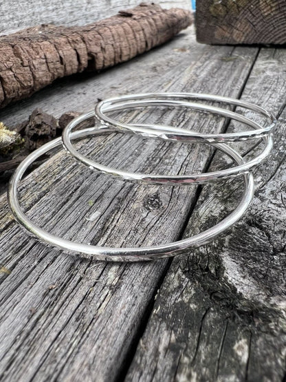 Multiple recycled sterling silver 3mm textured round bangles styled together on weathered wood