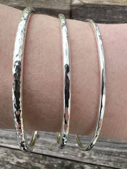 Three recycled sterling silver textured round bangles stacked on a wrist, showing how different sizes layer together