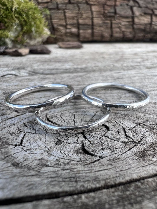Set of three recycled sterling silver textured stacking rings arranged on weathered wood with natural foliage