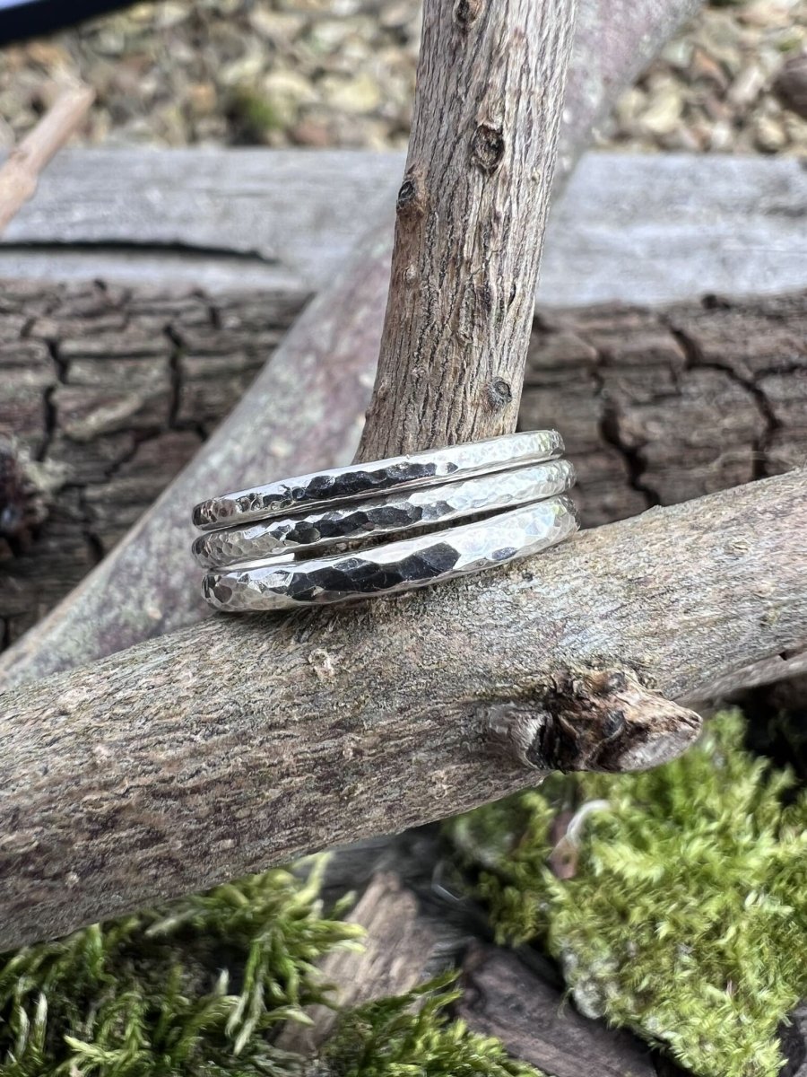 Textured recycled silver stacking rings resting on a mossy tree branch, styled flat lay
