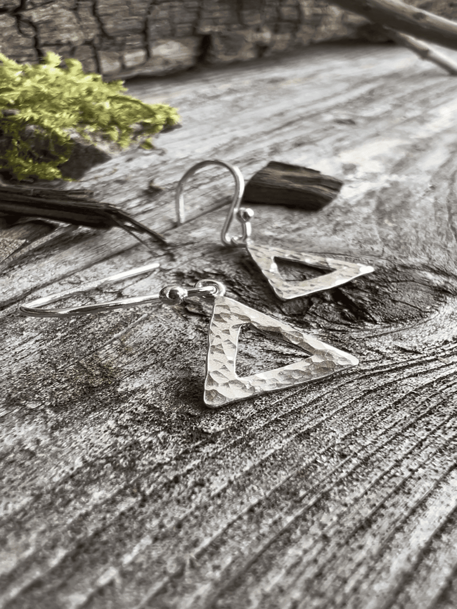 Close-up of handmade sterling silver textured triangle earrings on weathered wood, highlighting the hammered triangular frame