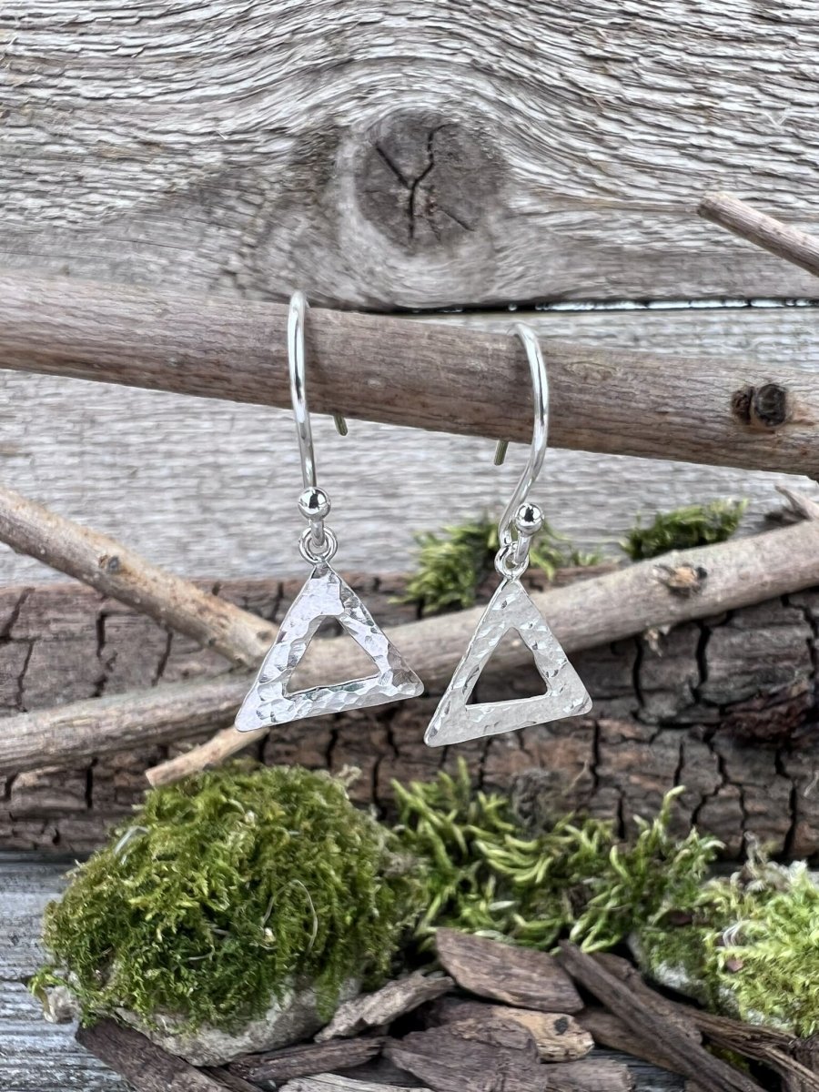 Recycled silver textured triangle drop earrings hanging from a branch with moss, showing the geometric design from the front