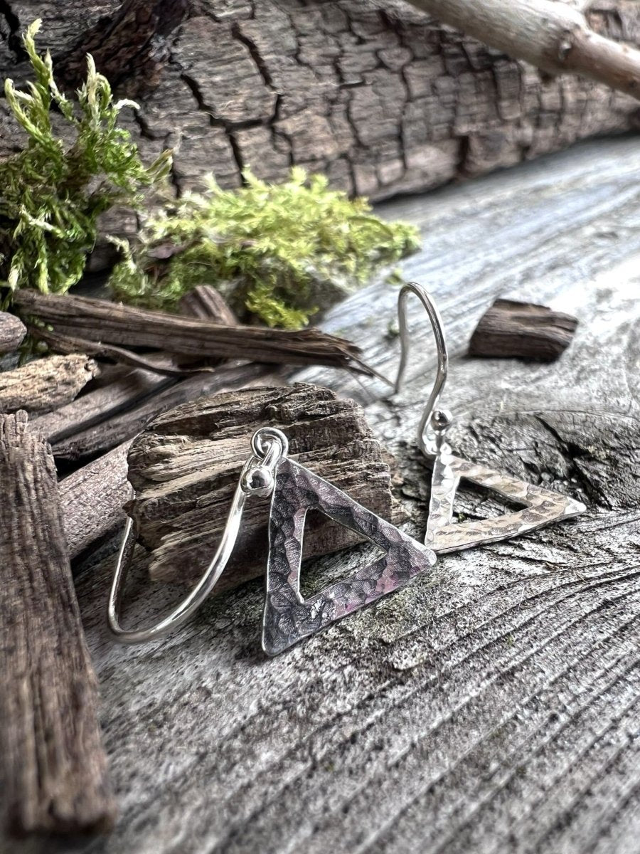 Handmade sterling silver textured triangle earrings on weathered wood with foliage, low angle showing the open triangle pendant