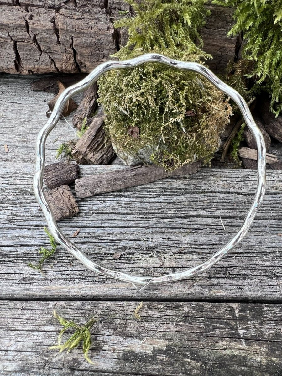 Handmade sterling silver 2.5mm wave bangle on mossy weathered wood, photographed from above showing the full rippled form