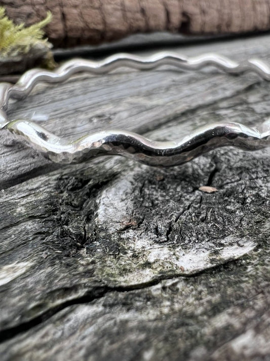 Close-up of a handmade sterling silver 3.5mm wave bangle on weathered wood, highlighting the rippled wave texture