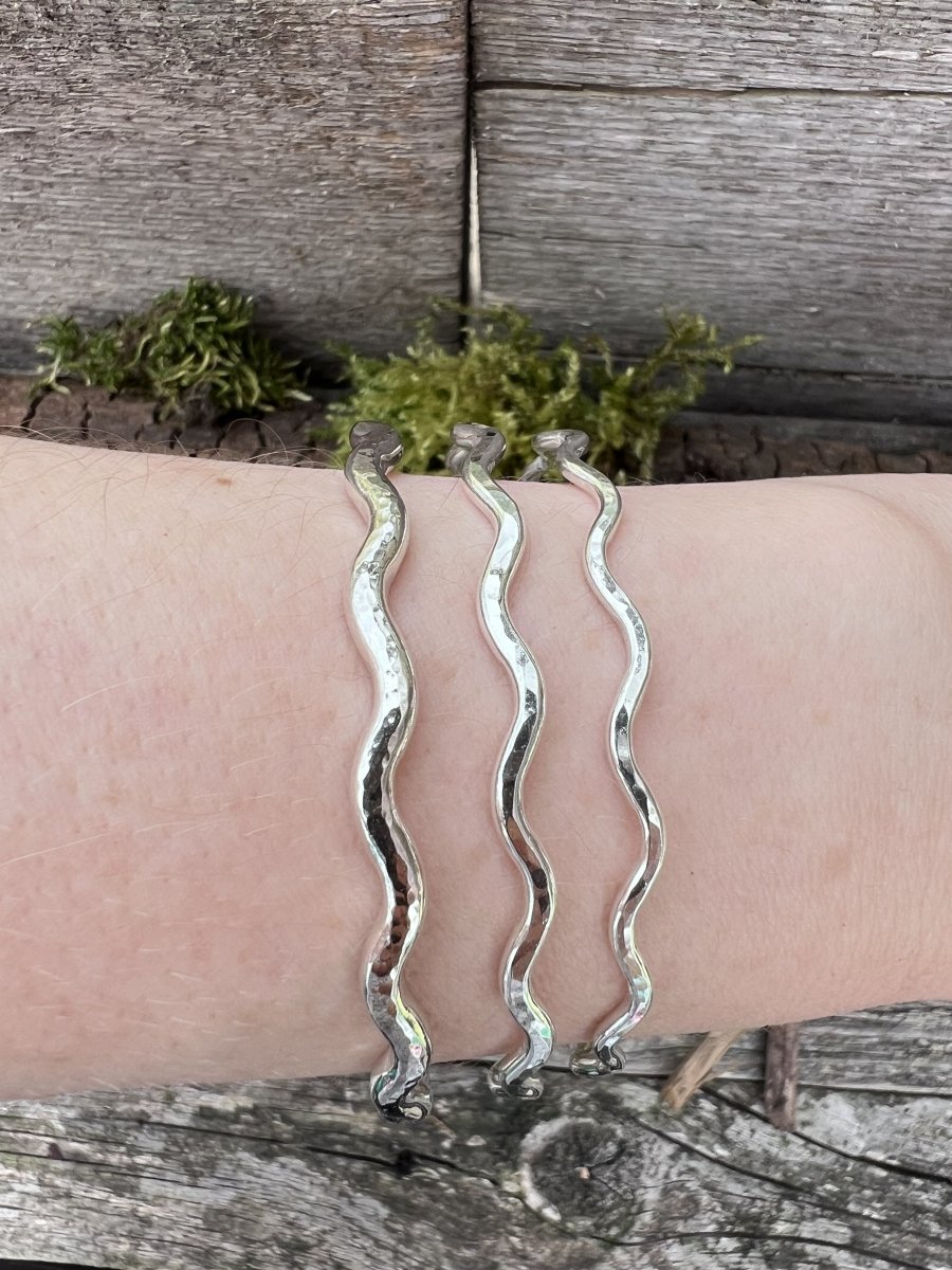 Three recycled sterling silver wave bangles stacked on a wrist, showing the different thicknesses layered together