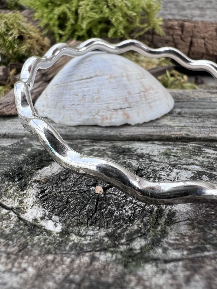 Recycled sterling silver 3.5mm wave bangle lying on weathered wood and shell, handmade Isle of Wight jewellery