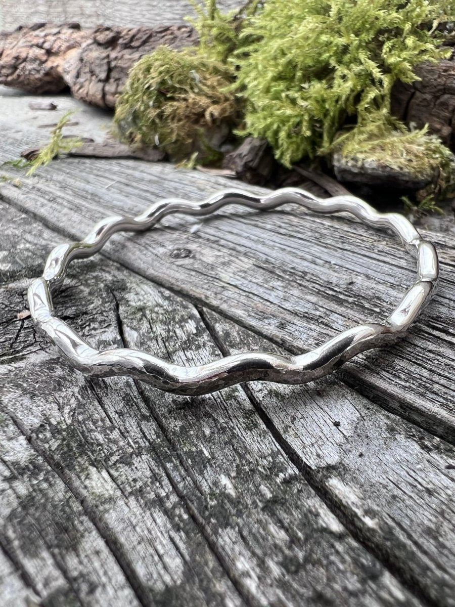 Handmade sterling silver 3.5mm wave bangle on mossy weathered wood, photographed from above showing the full wave form