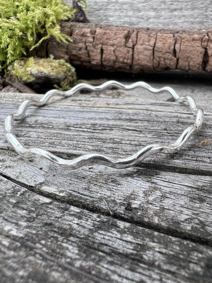 Recycled sterling silver wave bangle 3mm on weathered wood, showing the rippled wave-form band