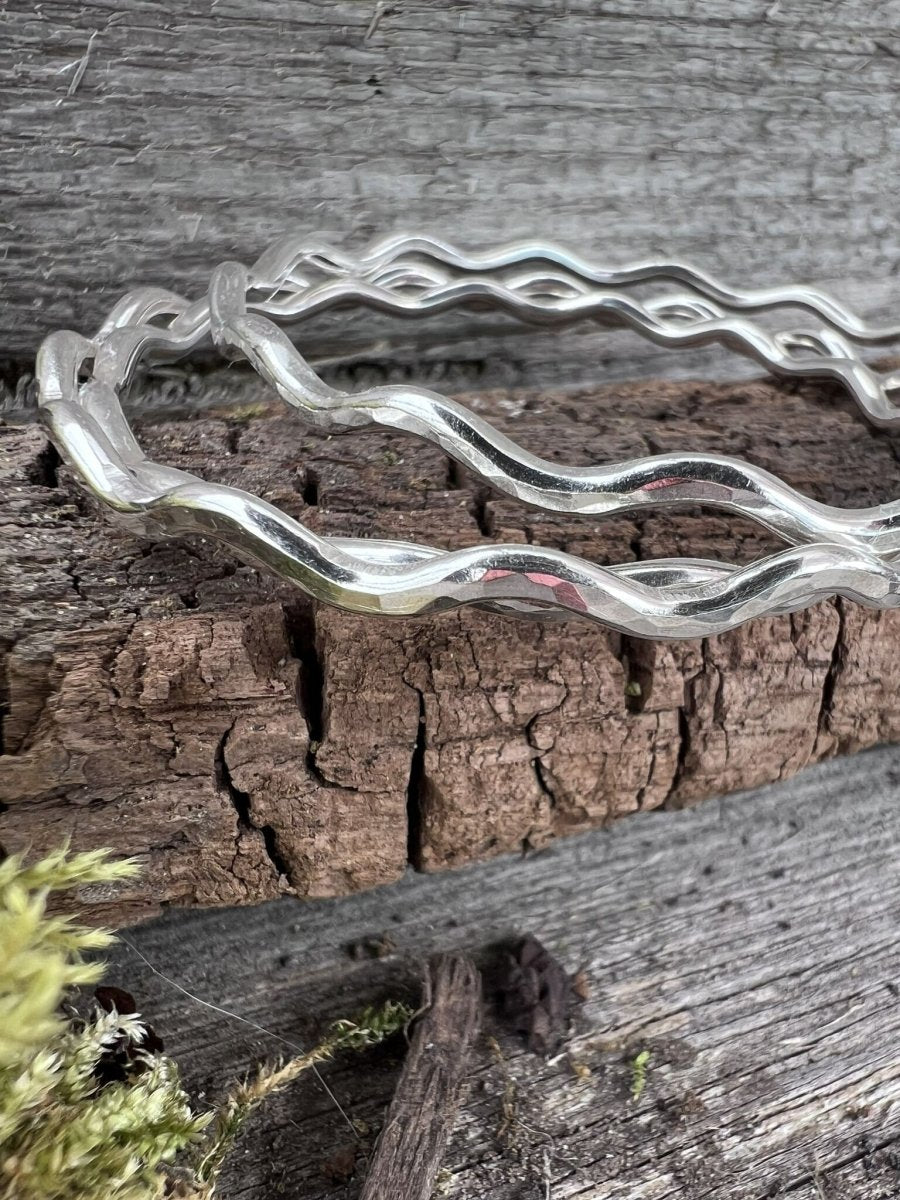 Close-up of three handmade sterling silver 3mm wave bangle on weathered wood, showing the undulating wave texture detail