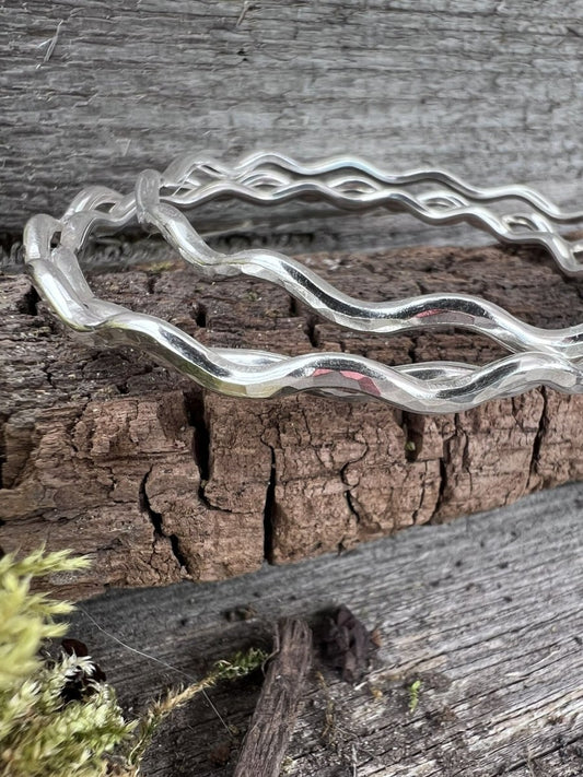 Close-up of three handmade sterling silver 3mm wave bangle on weathered wood, showing the undulating wave texture detail
