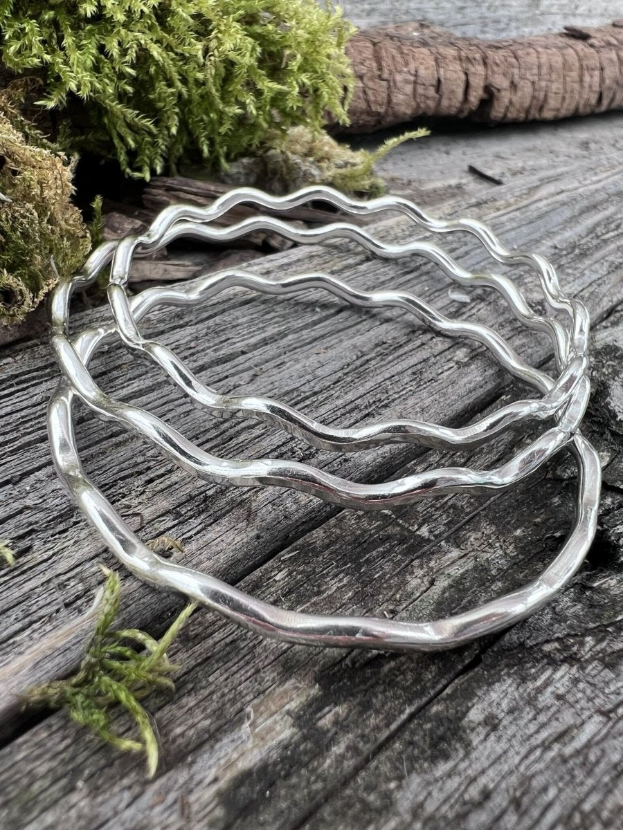 Recycled sterling silver 3mm wave bangles lying on weathered wood, handmade Isle of Wight jewellery