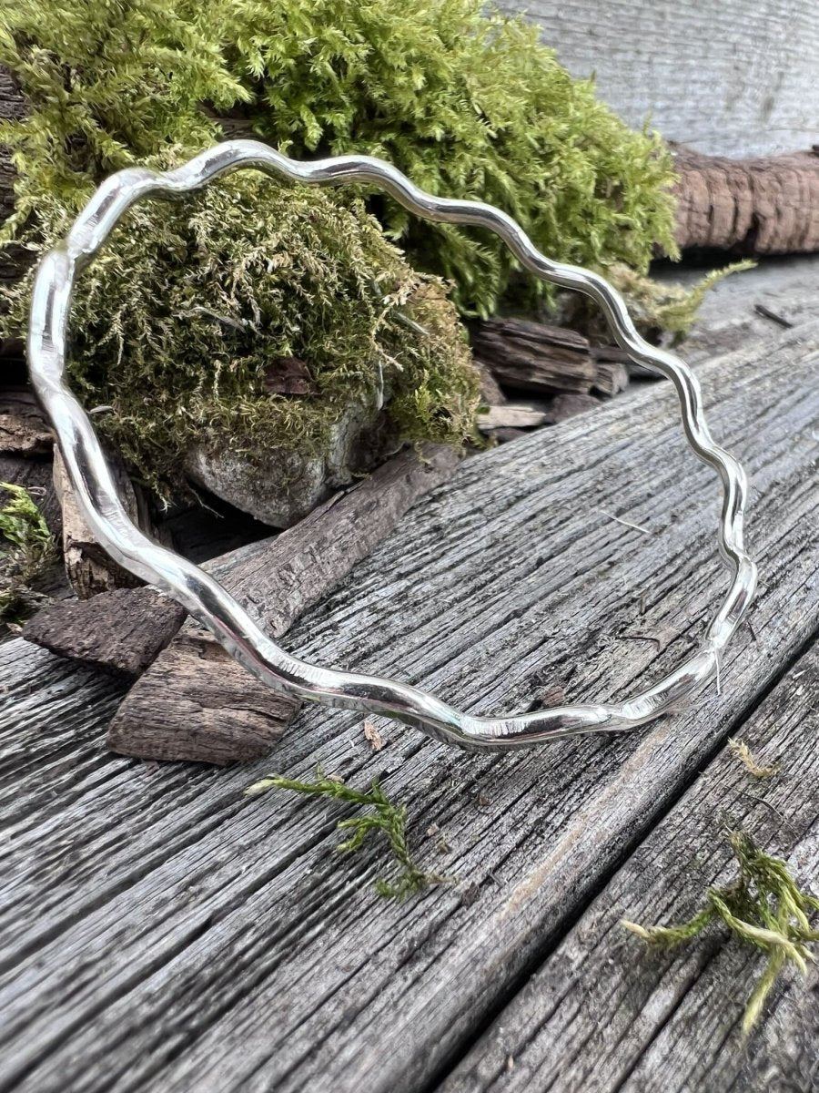 Handmade sterling silver 3mm wave bangle on mossy weathered wood, side angle showing the full circular wave form