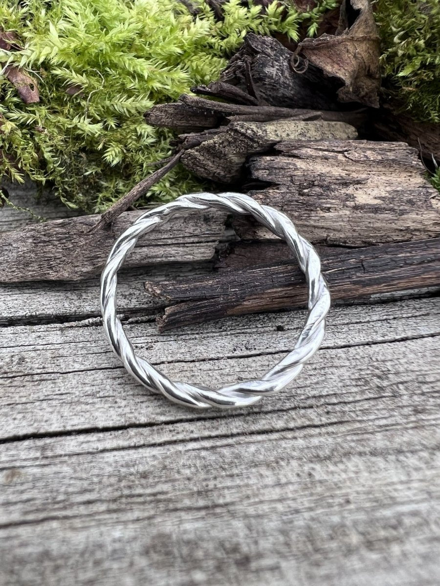 Handmade silver round twisted ring photographed flat on weathered wood, showing the full circular form