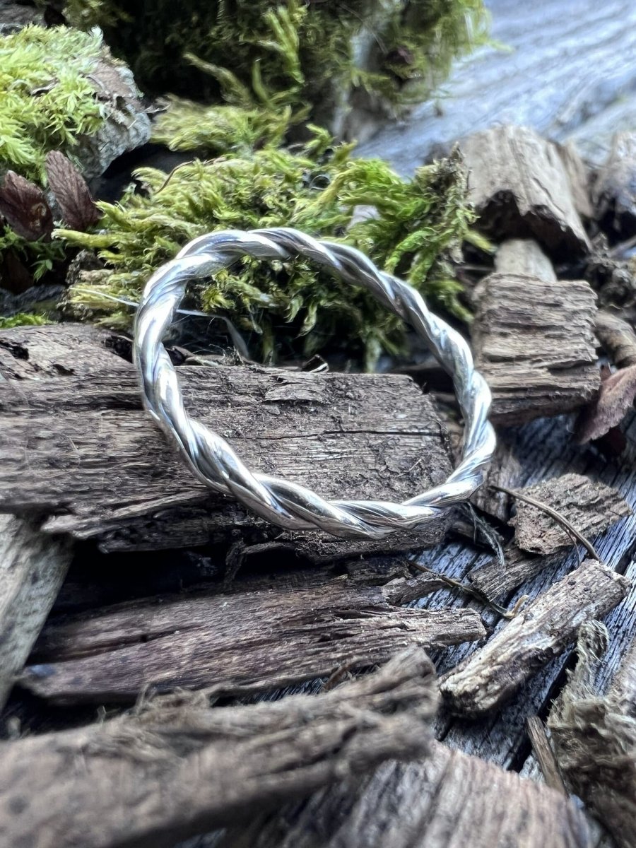 Close-up of a handmade sterling silver round twisted ring on weathered wood, showing the delicate twisted wire detail