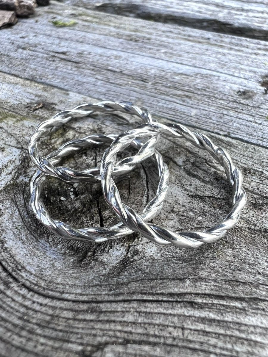 Multiple recycled silver round twisted rings arranged on weathered wood, styled together
