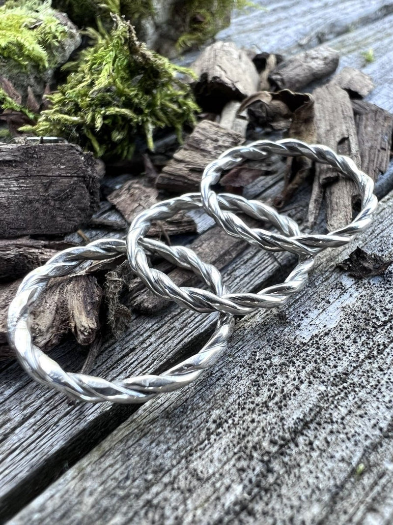 Recycled sterling silver round twisted rings resting on moss-covered weathered wood