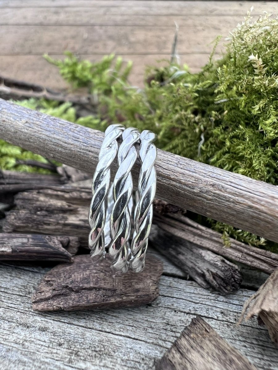Recycled sterling silver round twisted rings stacked on a wooden branch, handmade jewellery