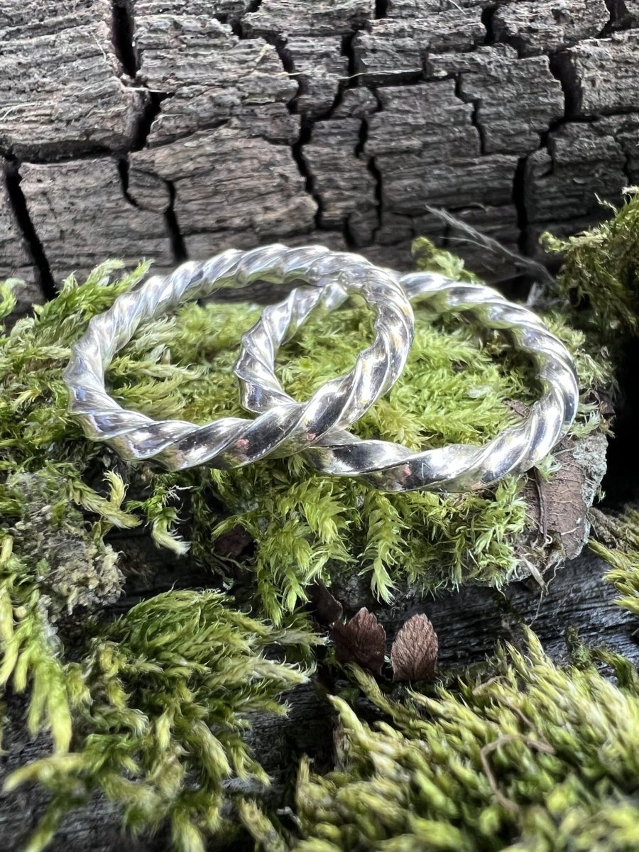 Handmade recycled silver square twist rings on moss and weathered stone, viewed from above