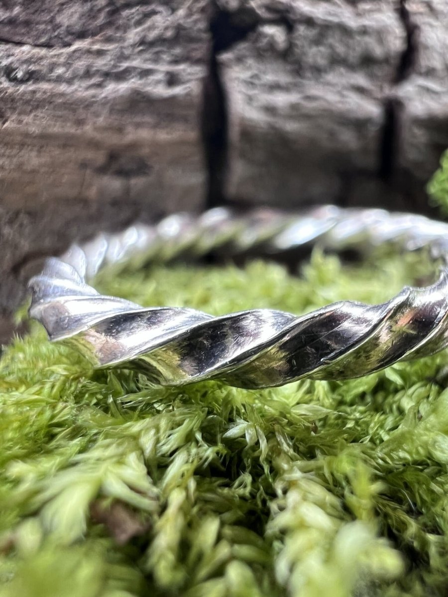 Close-up of a handmade silver square twist ring resting on green moss, highlighting the twisted texture