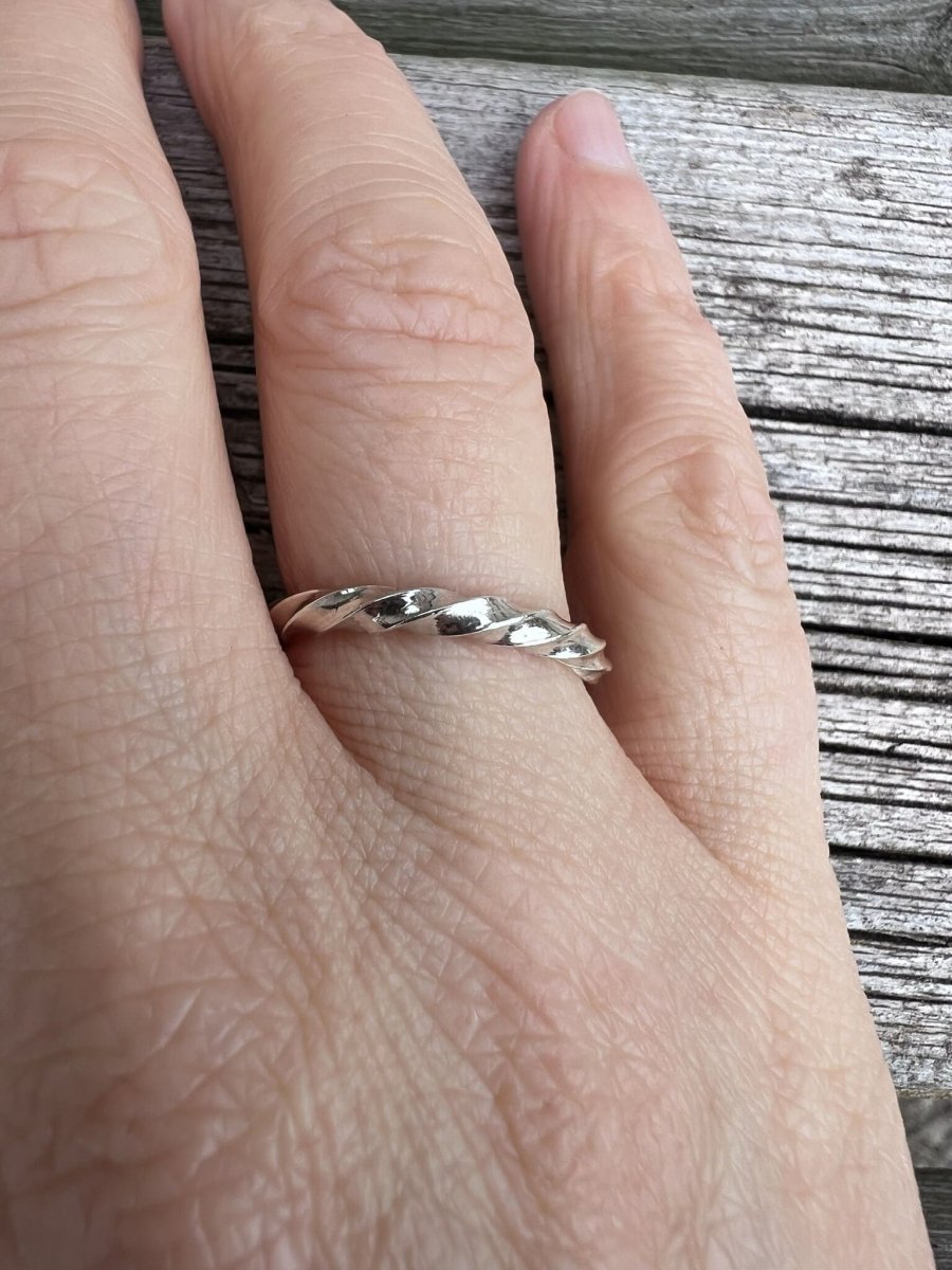Thin sterling silver square twist ring worn on a finger, showing the delicate twisted band and scale