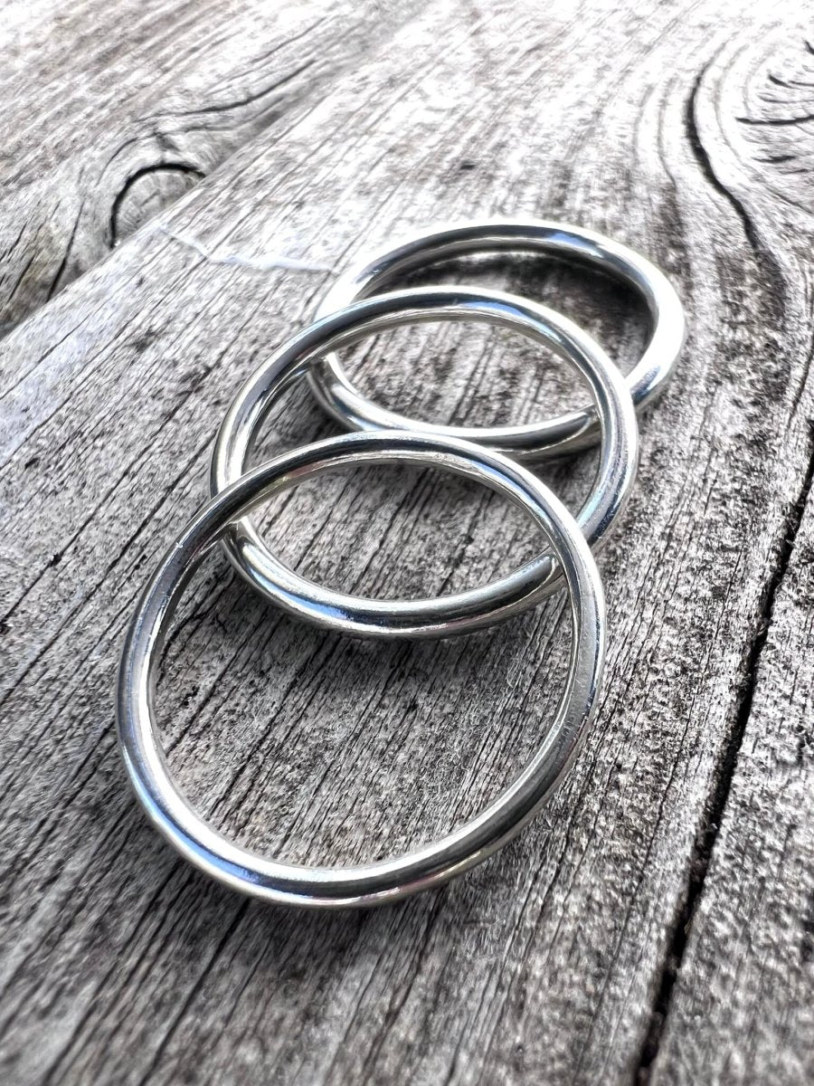 Slim handmade sterling silver stacking rings photographed from the side on weathered wood, showing their fine width