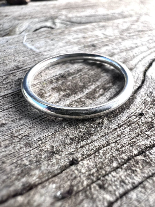 Close-up of a single thin sterling silver stacking ring on a wooden surface showing the fine, smooth band