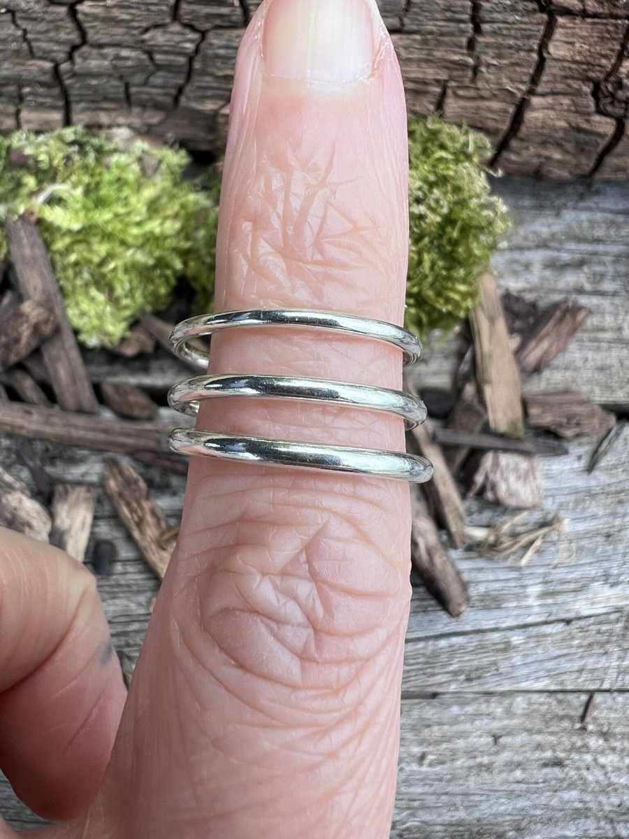 Three thin silver stacking rings worn on a finger alongside moss-covered stone, showing delicate scale