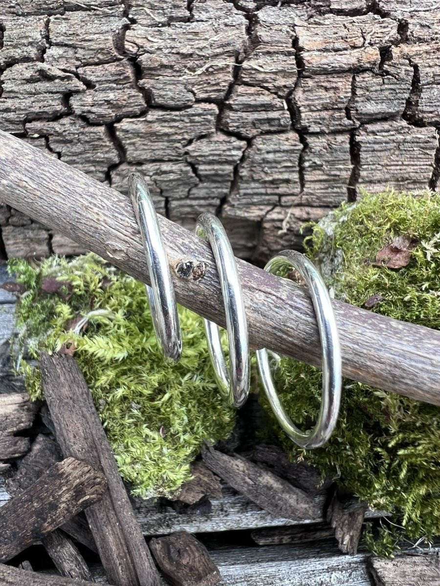 Thin recycled silver stacking rings hanging from a branch, styled with natural textures