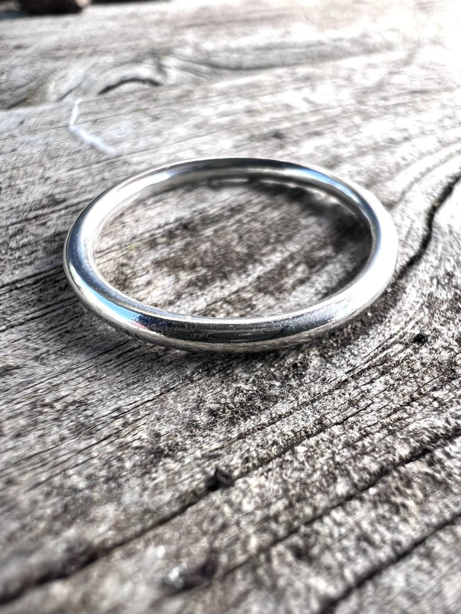 Close-up of a single thin sterling silver stacking ring on a wooden surface showing the fine, smooth band