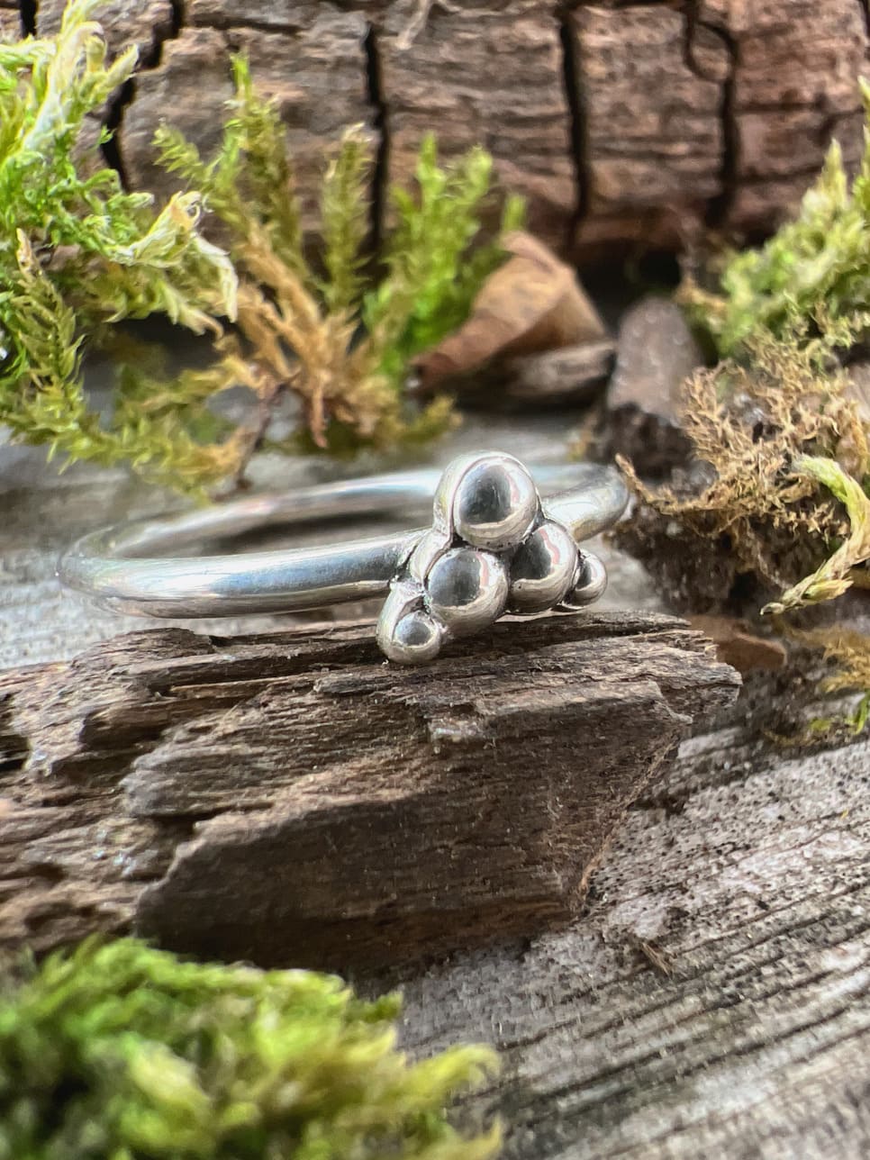 Close-up of a handmade sterling silver triple granule ring on mossy driftwood, showing the three fused silver beads