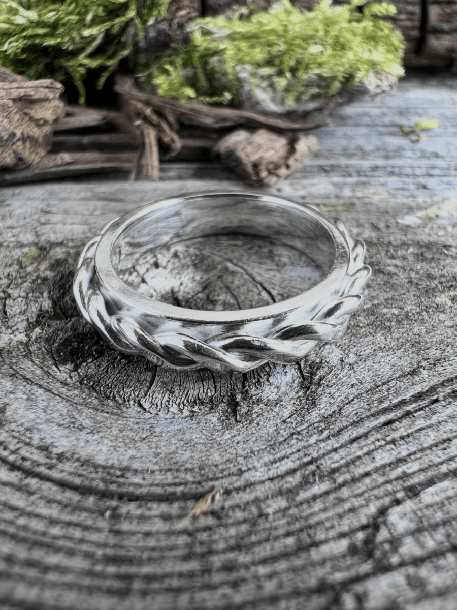 Recycled sterling silver twisted plait ring on a wooden surface with natural foliage, showing the plaited band detail