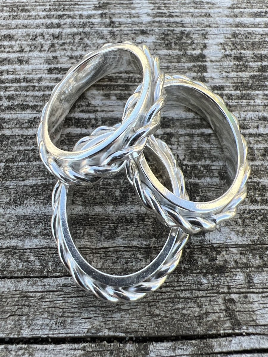 Two handmade sterling silver twisted plait rings photographed from an angle on weathered wood