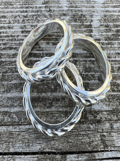Two handmade sterling silver twisted plait rings photographed from an angle on weathered wood