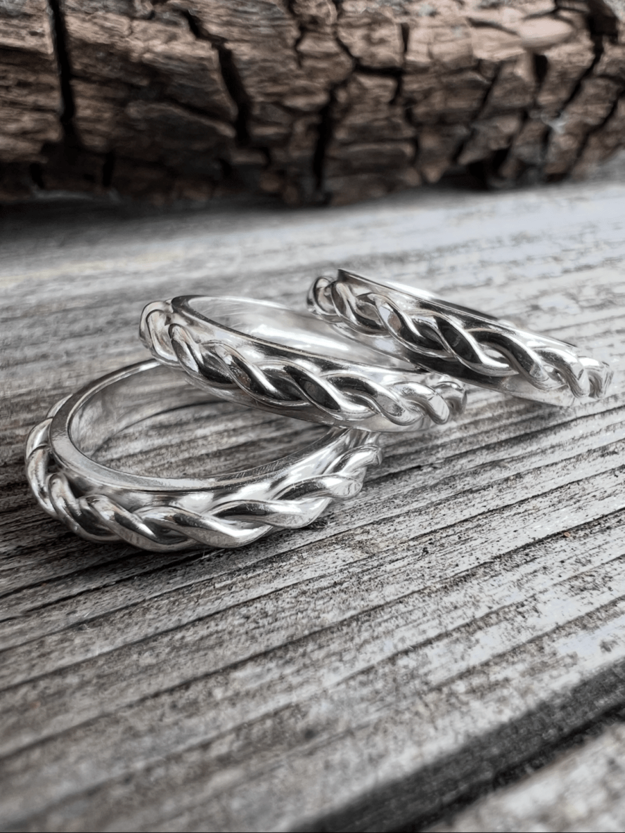 Close-up of two handmade sterling silver twisted plait rings on weathered wood, highlighting the woven plait texture