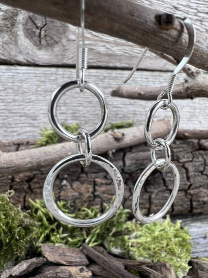 Close-up of handmade sterling silver unity drop earrings hanging from wooden branch, highlighting texture details