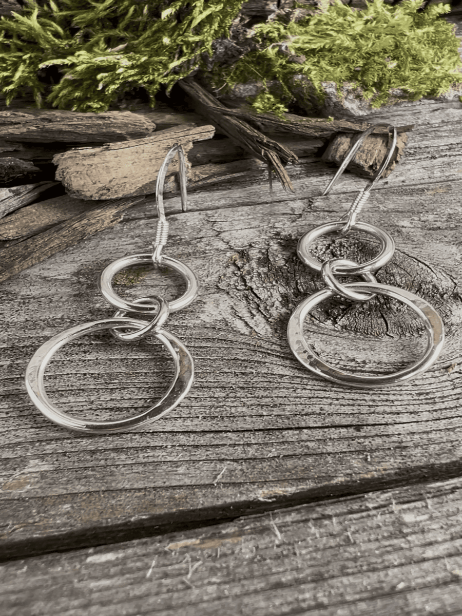 Handmade sterling silver unity drop earrings on weathered wood with foliage, photographed from an angle showing earring depth