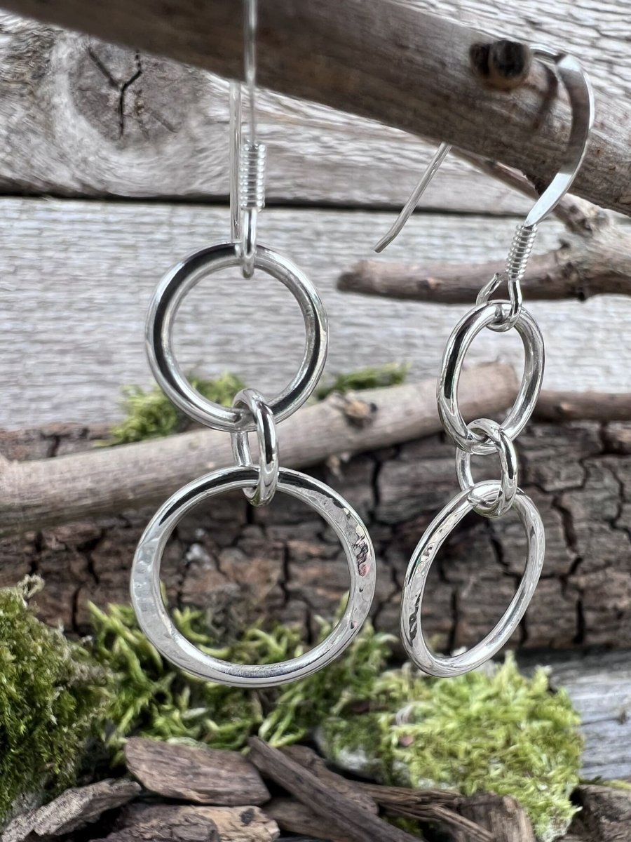 Close-up of handmade sterling silver unity drop earrings hanging from a branch, highlighting the three connected open circles