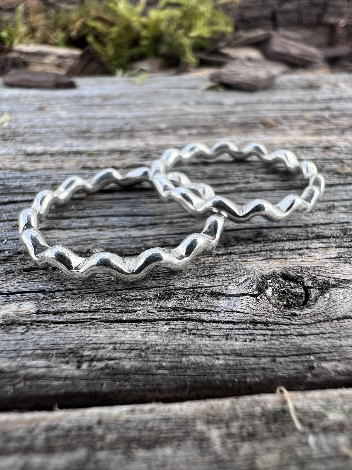 Handmade sterling silver wave ring on driftwood, side angle showing the wave edge profile of the band