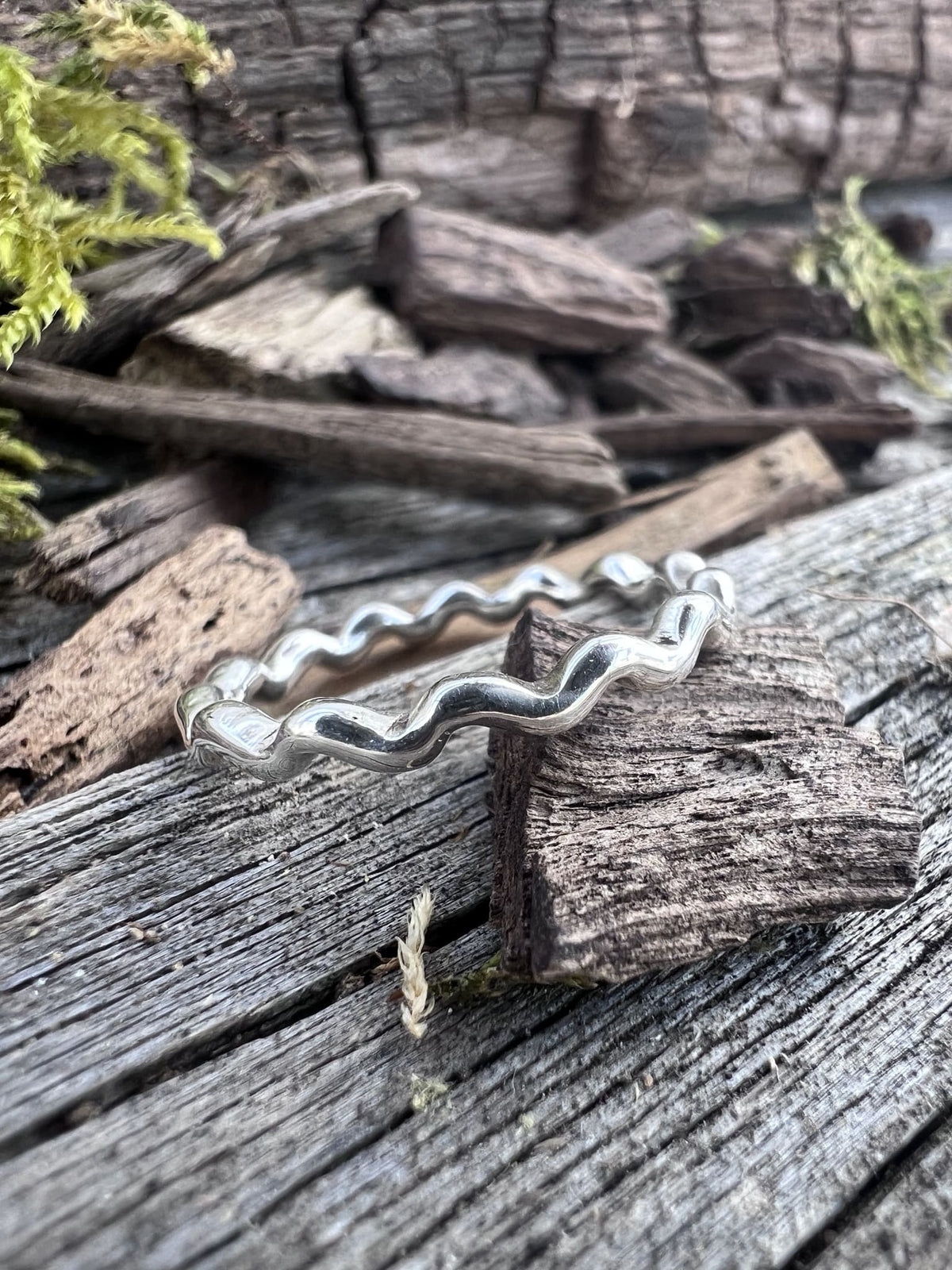 Recycled sterling silver wave ring on weathered driftwood, showing the undulating wave-edged band