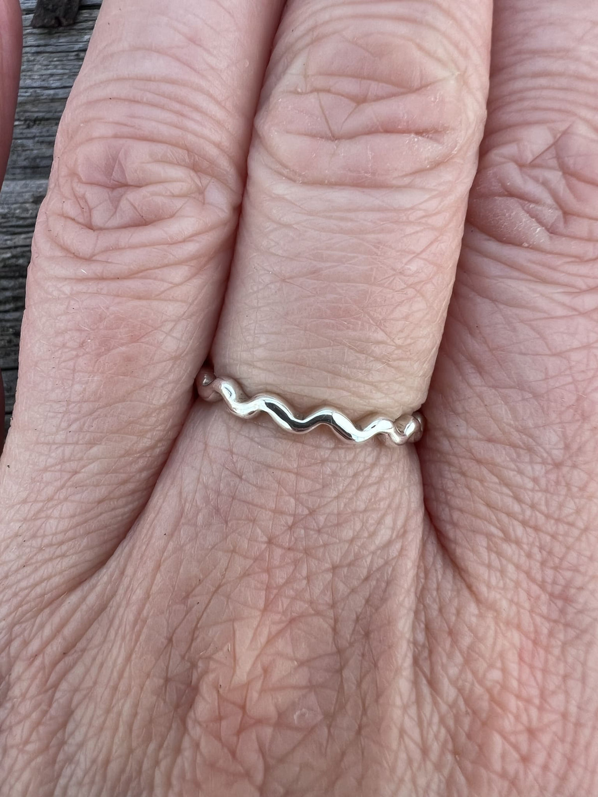 Sterling silver wave ring worn on a finger, showing scale and the delicate wave-edged band