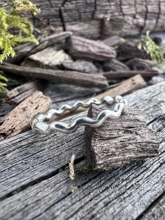 Recycled sterling silver wave ring on weathered driftwood, showing the undulating wave-edged band