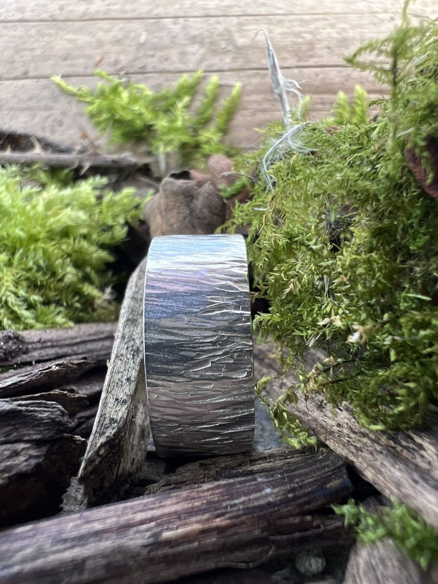 Wide band sterling silver bark texture ring styled with green foliage and wood chips, handmade Isle of Wight jewellery