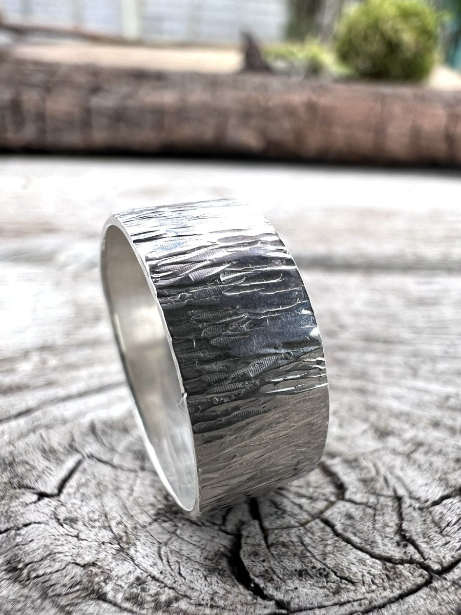 Recycled sterling silver wide band ring with bark texture on weathered wood, showing the linear engraved surface detail