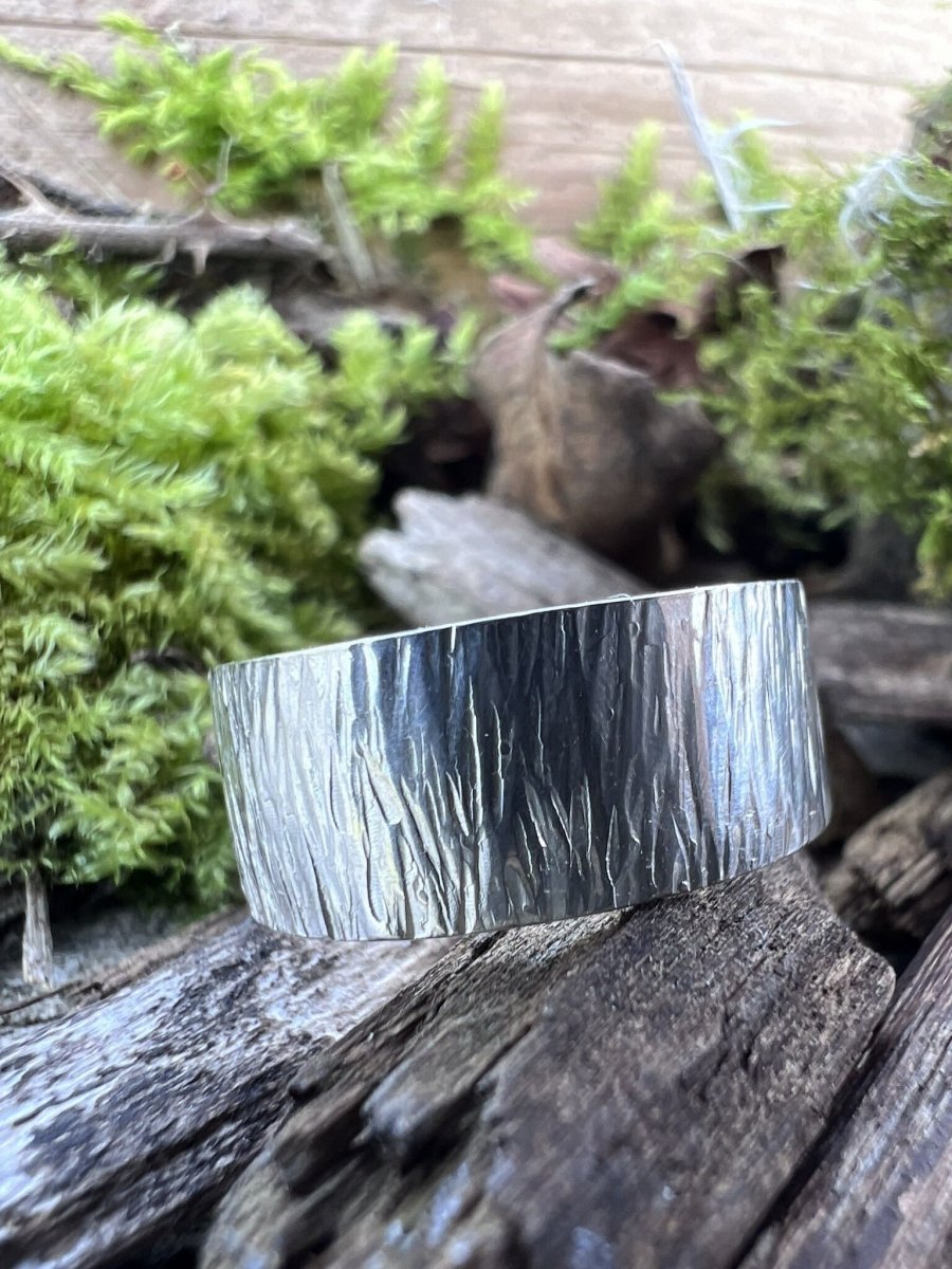 Recycled sterling silver wide band ring with bark texture on weathered wood, showing the linear engraved surface detail