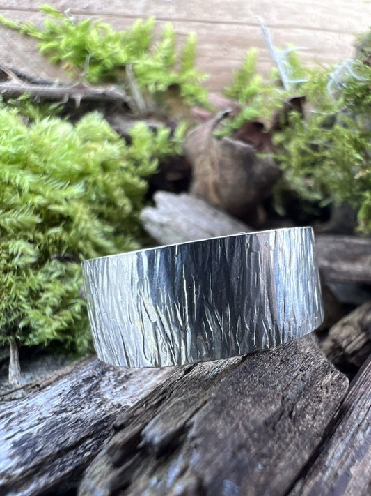 Recycled sterling silver wide band ring with bark texture on weathered wood, showing the linear engraved surface detail