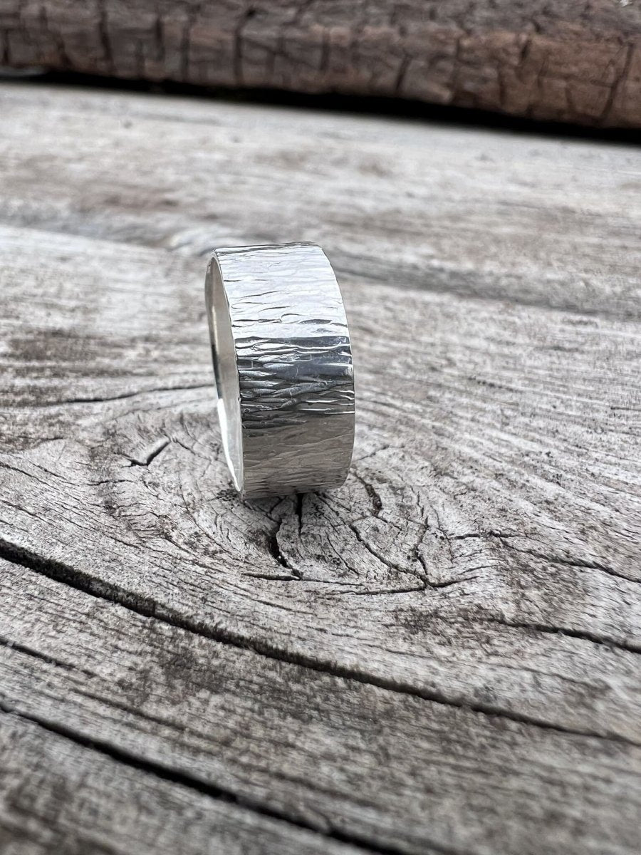 Handmade sterling silver wide band ring with bark texture photographed from a low angle on weathered wood, showing band depth