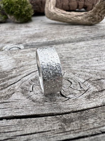 Recycled sterling silver wide band chipped texture ring standing upright on weathered wood with moss in the background