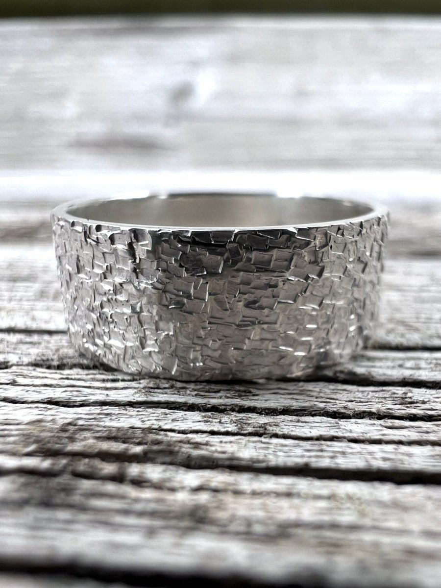 Handmade recycled silver wide band ring with chipped texture photographed side-on on weathered wood, showing the band width