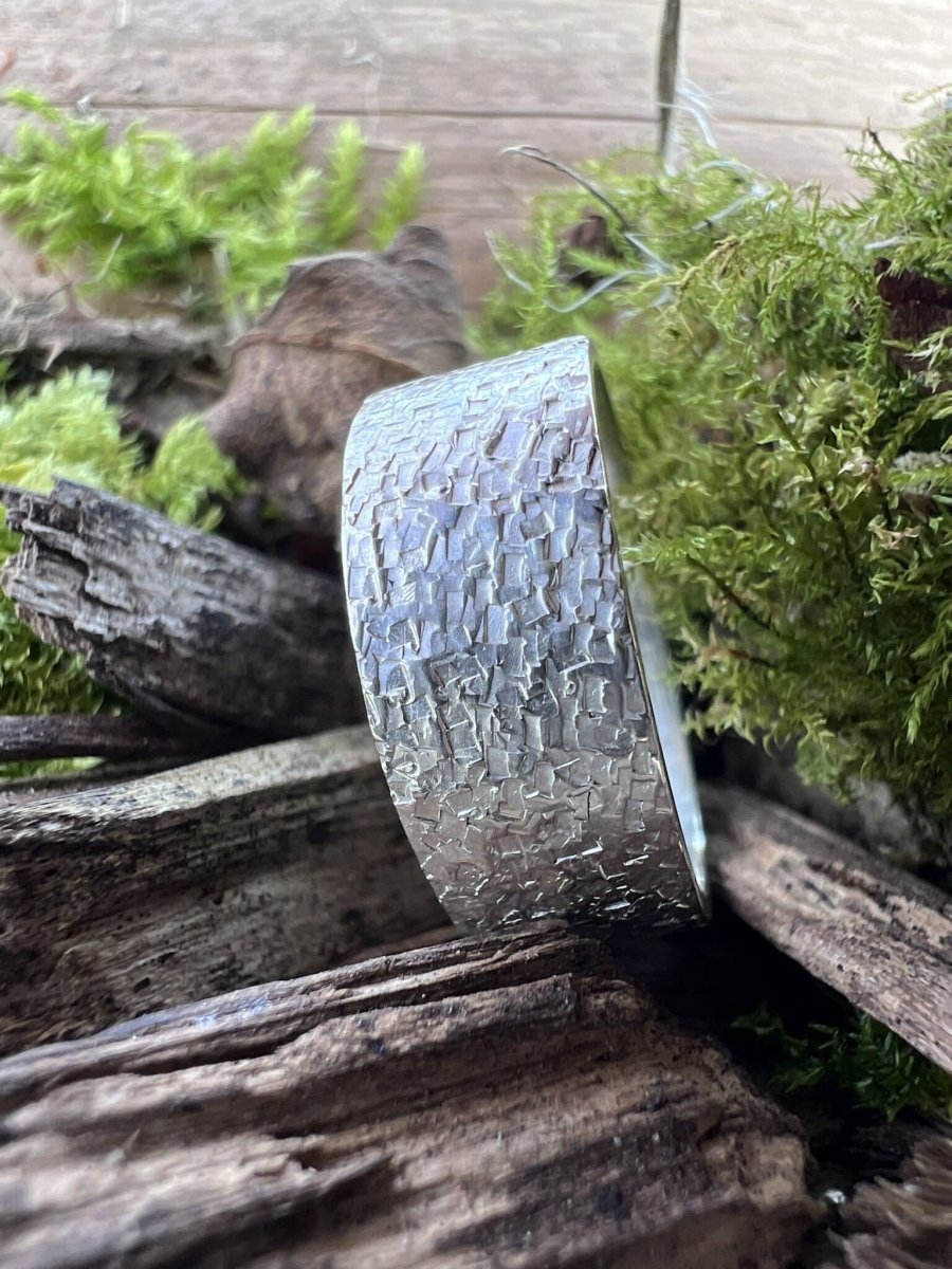 Wide band sterling silver ring with chipped texture styled on wood chips surrounded by natural foliage, Isle of Wight jewellery